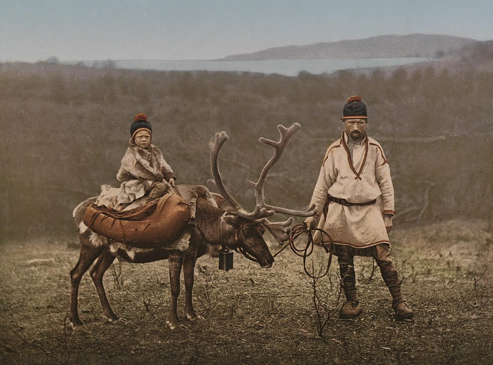 Saami man leading reindeer being ridden by a child