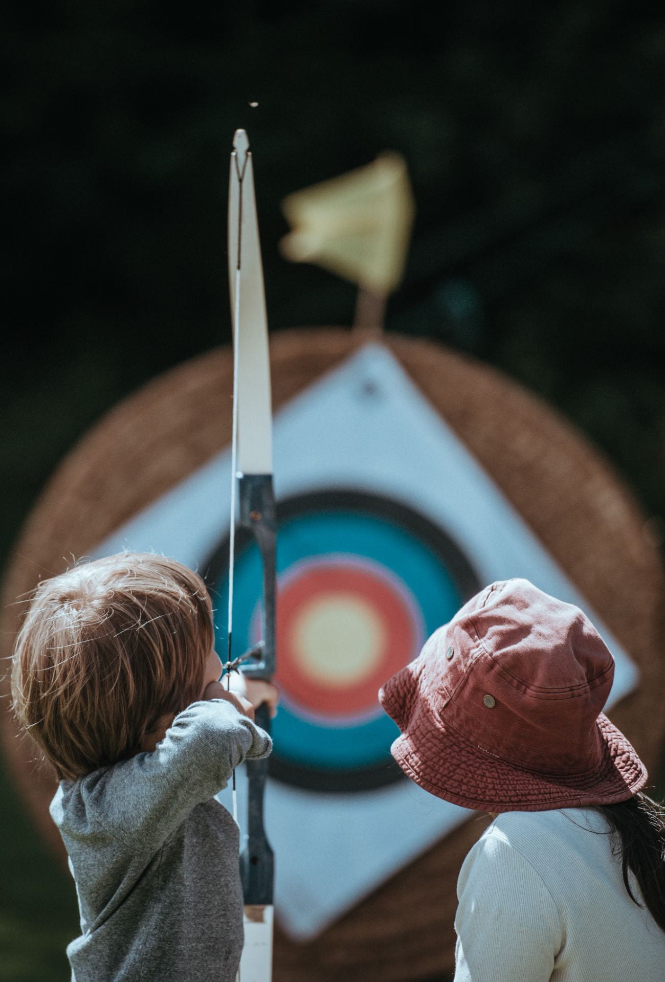 woman teaching boy to shoot arrow